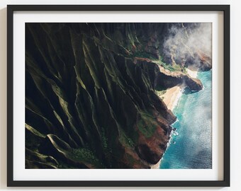 May include: An aerial view of a rugged coastline with lush green cliffs and a sandy beach. The turquoise ocean water crashes against the rocky shore.