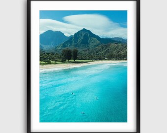 Puede incluir: Vista aérea de una playa con agua turquesa y una cordillera de montañas en el fondo. El agua es clara y tranquila, y hay algunas personas surfeando en la distancia.