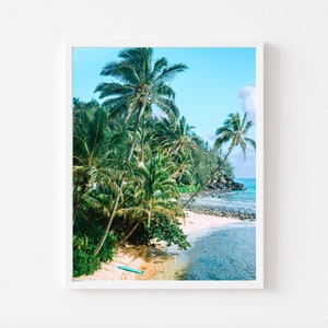 May include: A photograph of a tropical beach scene with palm trees, a sandy shore, and turquoise water. A blue surfboard lies on the sand.
