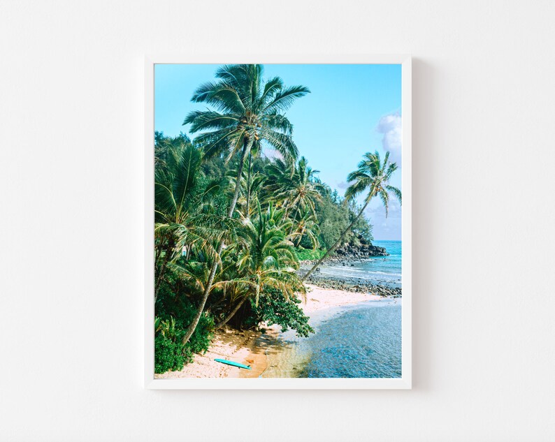 May include: A photograph of a tropical beach scene with palm trees, a sandy shore, and turquoise water. A blue surfboard lies on the sand.