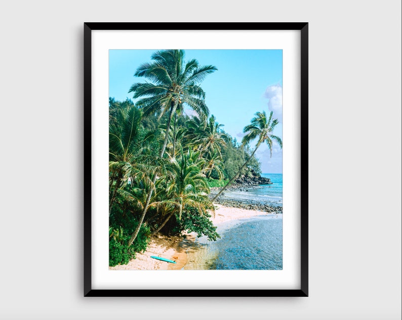 May include: A photograph of a tropical beach scene with palm trees, a sandy shore, and turquoise water. A blue surfboard lies on the sand.