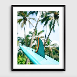 May include: A turquoise surfboard fin with an orange stripe against a backdrop of palm trees.