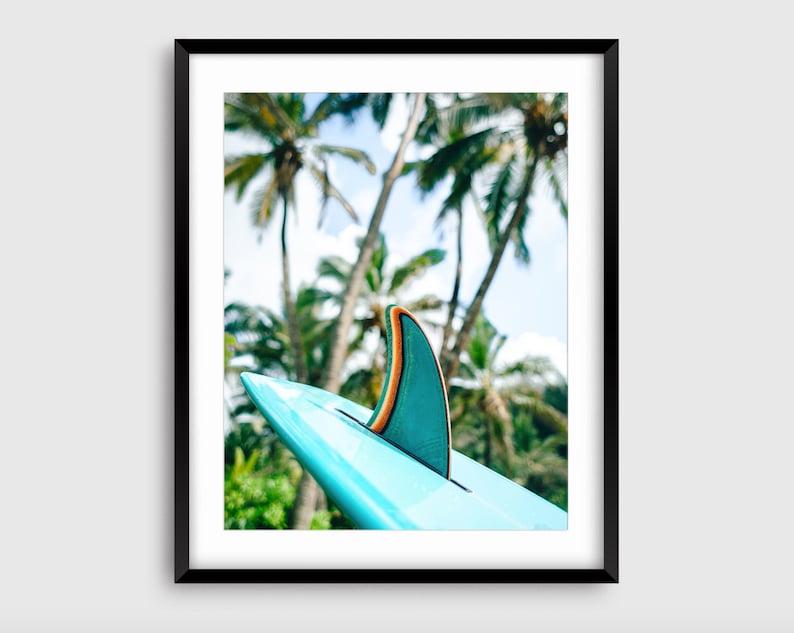 May include: A turquoise surfboard fin with an orange stripe against a backdrop of palm trees.