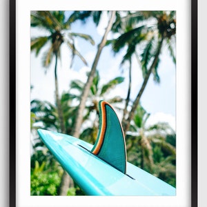K&ouml;nnte beinhalten: Eine blaue Surfboard-Finne mit einem gr&uuml;nen und orangefarbenen Streifen vor einem Hintergrund aus Palmen.