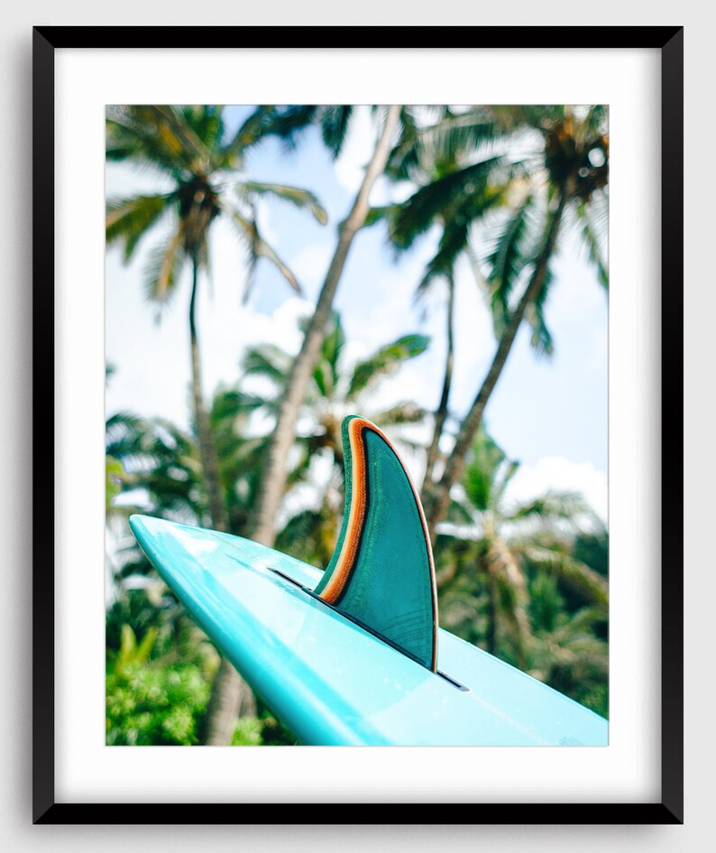K&ouml;nnte beinhalten: Eine blaue Surfboard-Finne mit einem gr&uuml;nen und orangefarbenen Streifen vor einem Hintergrund aus Palmen.