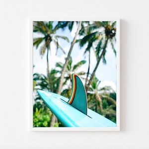May include: A teal surfboard fin with an orange stripe against a backdrop of palm trees.