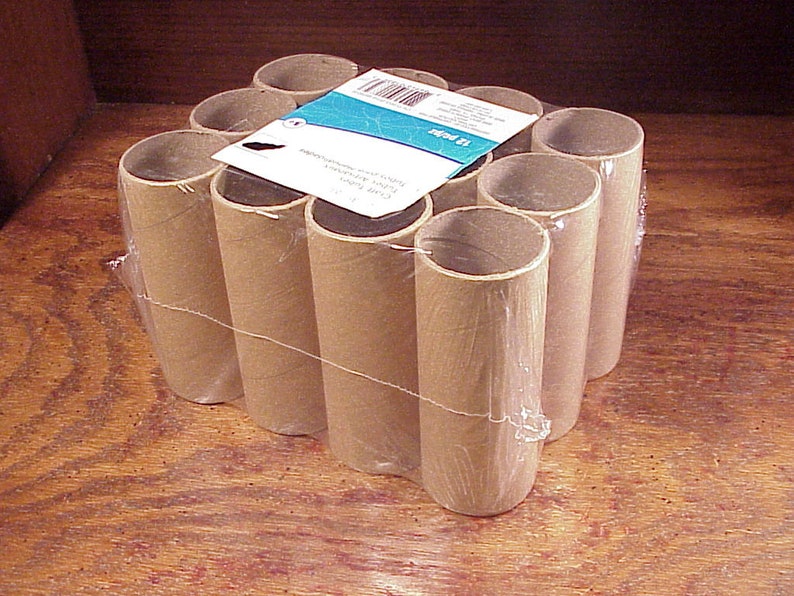 May include: A pack of 12 brown cardboard tubes, wrapped in clear plastic. The tubes are arranged in a rectangular shape. The pack has a label that reads "Craft Paper Tubes, 12 Pack, 3 Inch x 12 Inch".
