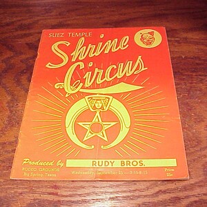 May include: A vintage poster advertising a Shrine Circus produced by Rudy Bros. at the Rodeo Grounds in Big Spring, Texas on Wednesday, September 25th, 1915. The poster features a red background with a yellow star and crescent moon design, and the text "Shrine Circus" in a large, stylized font.