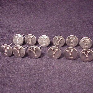 May include: Twelve silver-toned metal tacks with a decorative Y design. Each tack has a sharp point for attaching to a surface.