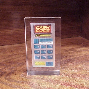 May include: A clear acrylic block with a blue and white image of a keypad with the text "CASH CODE" and "DO NOT REMOVE" printed on it. The keypad has a number display that reads "000040-013".