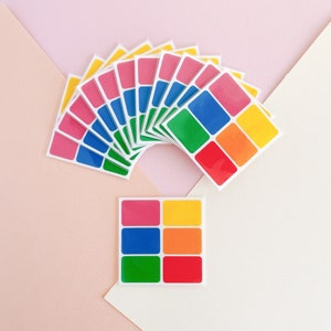 May include: A set of colourful square stickers with a rainbow pattern. The stickers are arranged in a fan shape and are ready to be used for crafts, scrapbooking, or decorating.