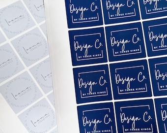 以下が含まれることがあります： 「Design Co. by Three Kings」というテキストが書かれた、青と白の正方形のステッカーのシートです。