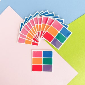 May include: A set of colourful stickers in a rainbow pattern. The stickers are arranged in a fan shape and are on a pink, blue and green background.