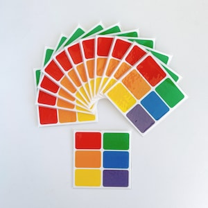 May include: A set of rainbow coloured adhesive stickers arranged in a semi-circle. The stickers are in the order of the rainbow, with red at the top and violet at the bottom. The stickers are arranged in a semi-circle, with the red sticker at the top and the violet sticker at the bottom. The stickers are all the same size and shape, and they are all rectangular.