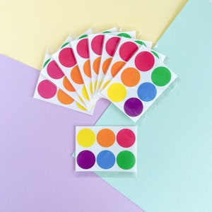 Può includere: Un set di adesivi rotondi colorati con uno schema di colori arcobaleno. Gli adesivi sono disposti a ventaglio e sono pronti per essere utilizzati per l'artigianato, la decorazione o l'etichettatura.