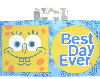 May include: Two yellow square stickers with a blue background. One sticker features a cartoon character with a yellow face, blue eyes, and a big smile. The other sticker has a yellow circle with the text "Best Day Ever" in blue letters.