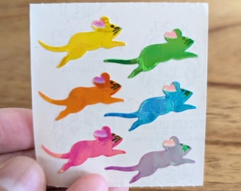 May include: A sheet of colorful mouse stickers. The stickers are iridescent and feature a variety of colors, including yellow, green, orange, blue, pink, and purple. Each mouse has a pink heart on its head.