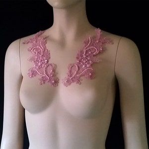 May include: Two pink lace appliques with beaded embellishments. The appliques are shaped like floral designs and are perfect for adding a touch of elegance to any garment.