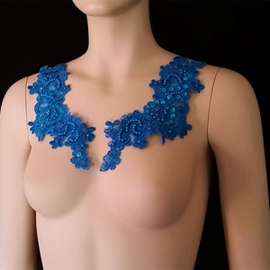 May include: A pair of blue lace appliques with pearl and sequin embellishments. The appliques are shaped like a V and are perfect for adding a touch of elegance to any garment.