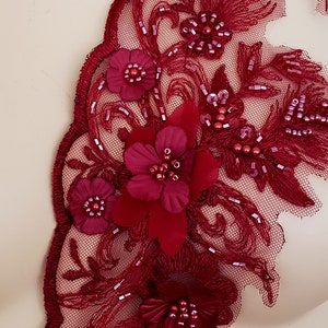 May include: Burgundy red lace applique with beaded flowers and leaves. The applique is made of delicate lace and features a floral design with small, round beads.