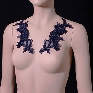 May include: Two black lace appliques with a floral design. The appliques are made of delicate lace and have a scalloped edge.