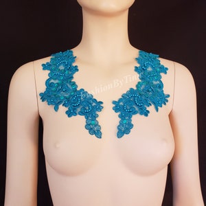 May include: Teal lace applique with floral and scroll designs, embellished with teal beads. The applique is displayed on a mannequin, showcasing its shape and detail. Perfect for embellishing garments or accessories.