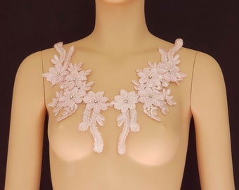 May include: A delicate pink lace applique with floral designs and small pearl-like embellishments. This applique is perfect for adding a touch of elegance to clothing or crafts.