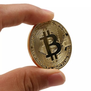 以下が含まれることがあります： 中央に黒いビットコインのシンボルが描かれた金色のビットコインコイン。コインは、複雑なディテールが施された円形のデザインで、縁には「Bitcoin Decentralized Peer to Peer」という文字が刻まれています。