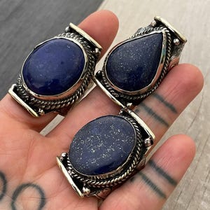Op de afbeelding: Drie zilveren ringen met blauwe lapis lazuli edelstenen. De ringen hebben ingewikkelde ontwerpen en worden aan een vinger gedragen.