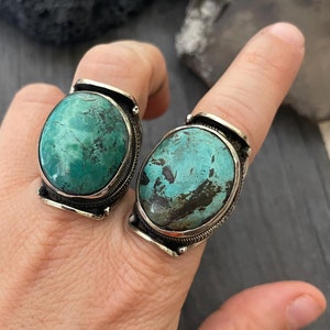 May include: Two silver rings with turquoise stones. The stones are oval shaped and have a green and blue colour.