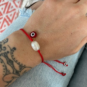 May include: Red string bracelet with a white pearl charm and a blue evil eye charm.