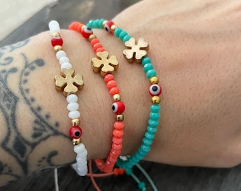 May include: Three bracelets with gold clover charms and evil eye beads. The bracelets are white, coral, and turquoise.