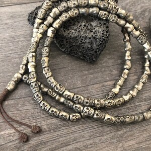 May include: A silver skull bead necklace with a dark brown cord. The necklace is made of many small skull beads that are all connected together.