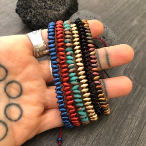 May include: A set of six beaded bracelets in various colors, including blue, red, turquoise, gold, black, and brown. The bracelets are stacked on top of each other and are made of small, round beads.