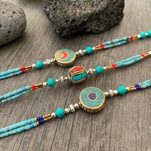 Puede incluir: Tres collares de cuentas turquesa y plata con colgantes redondos decorativos. Los colgantes est&aacute;n hechos de lat&oacute;n y presentan dise&ntilde;os intrincados con piedras turquesa, rojas y azules.