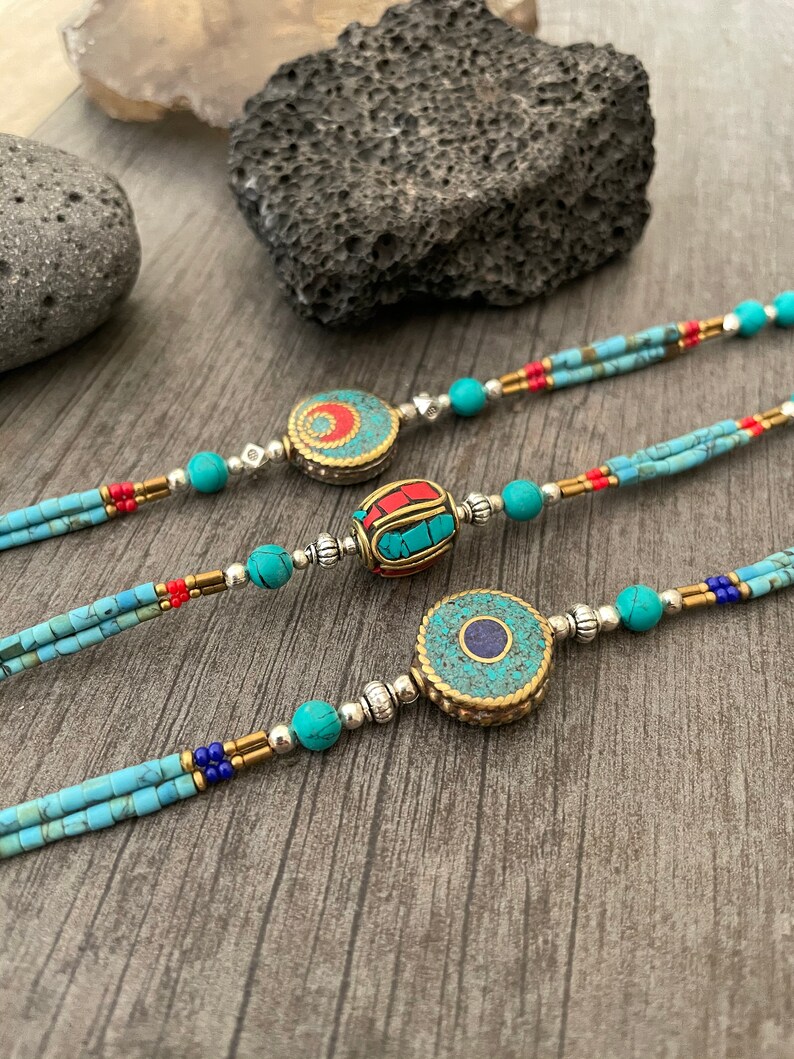 Puede incluir: Tres collares de cuentas turquesa y plata con colgantes redondos decorativos. Los colgantes est&aacute;n hechos de lat&oacute;n y presentan dise&ntilde;os intrincados con piedras turquesa, rojas y azules.