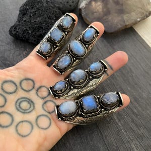 May include: Three silver rings with moonstone gemstones. Each ring has three stones set in a curved band with intricate details.