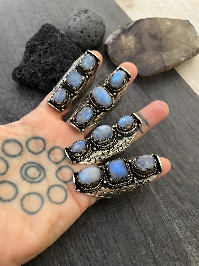 May include: Three silver rings with moonstone gemstones. Each ring has three stones set in a curved band with intricate details.