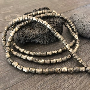 May include: A silver skull bead necklace with multiple strands of beads. The beads are small and round with a skull design on each bead.