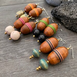 May include: Handmade wooden earrings with a variety of bead accents. The earrings feature brown, oval-shaped wooden beads wrapped with colorful thread, paired with round, speckled, and blue-green beads. The earrings have silver-colored hooks.
