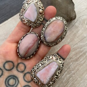 May include: Four silver rings with pink and white gemstone inlays. The rings have intricate designs and are set in a silver band.
