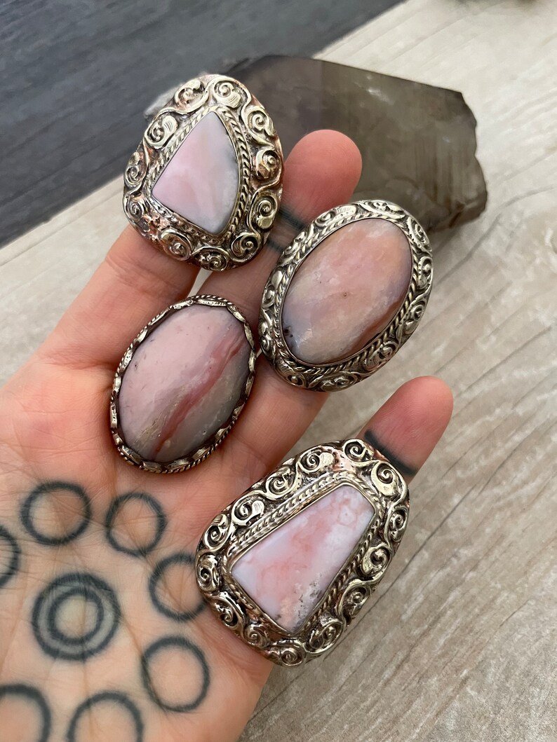 May include: Four silver rings with pink and white gemstone inlays. The rings have intricate designs and are set in a silver band.