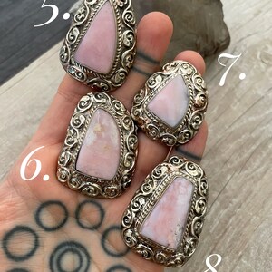 May include: Four pink opal rings with silver settings. The rings are set in a swirling, ornate design. The rings are numbered 5, 6, 7, and 8.