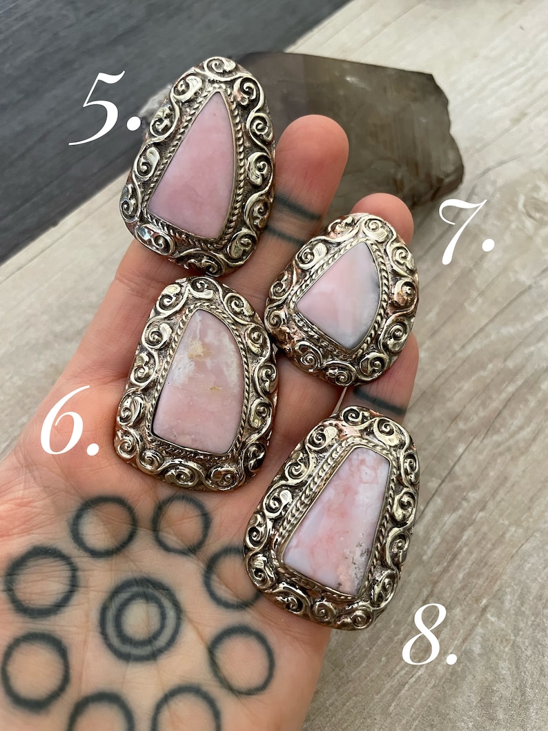 May include: Four pink opal rings with silver settings. The rings are set in a swirling, ornate design. The rings are numbered 5, 6, 7, and 8.