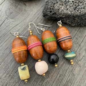 May include: Four pairs of handcrafted wooden earrings. Each earring features a wooden oval bead with colorful accents, including orange, pink, and green bands. The earrings have unique stone or bead drops in yellow, pink, black, and blue.
