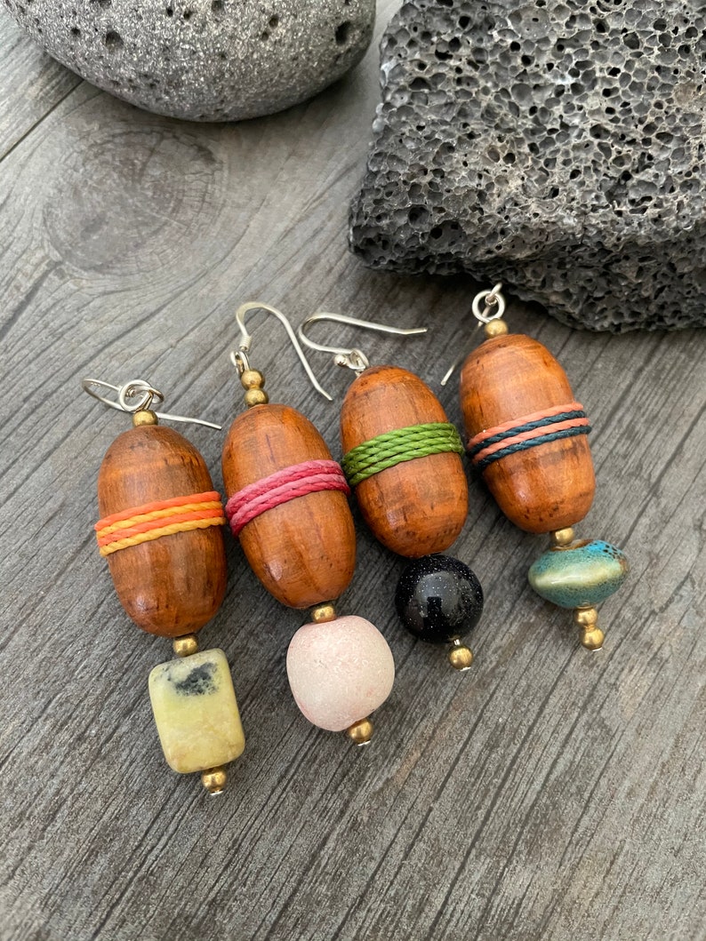 May include: Four pairs of handcrafted wooden earrings. Each earring features a wooden oval bead with colorful accents, including orange, pink, and green bands. The earrings have unique stone or bead drops in yellow, pink, black, and blue.