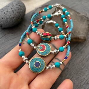 Puede incluir: Tres pulseras de cuentas turquesa con detalles plateados y dorados. Cada pulsera presenta un amuleto circular &uacute;nico con dise&ntilde;os intrincados y piedras turquesa, rojas y azules.