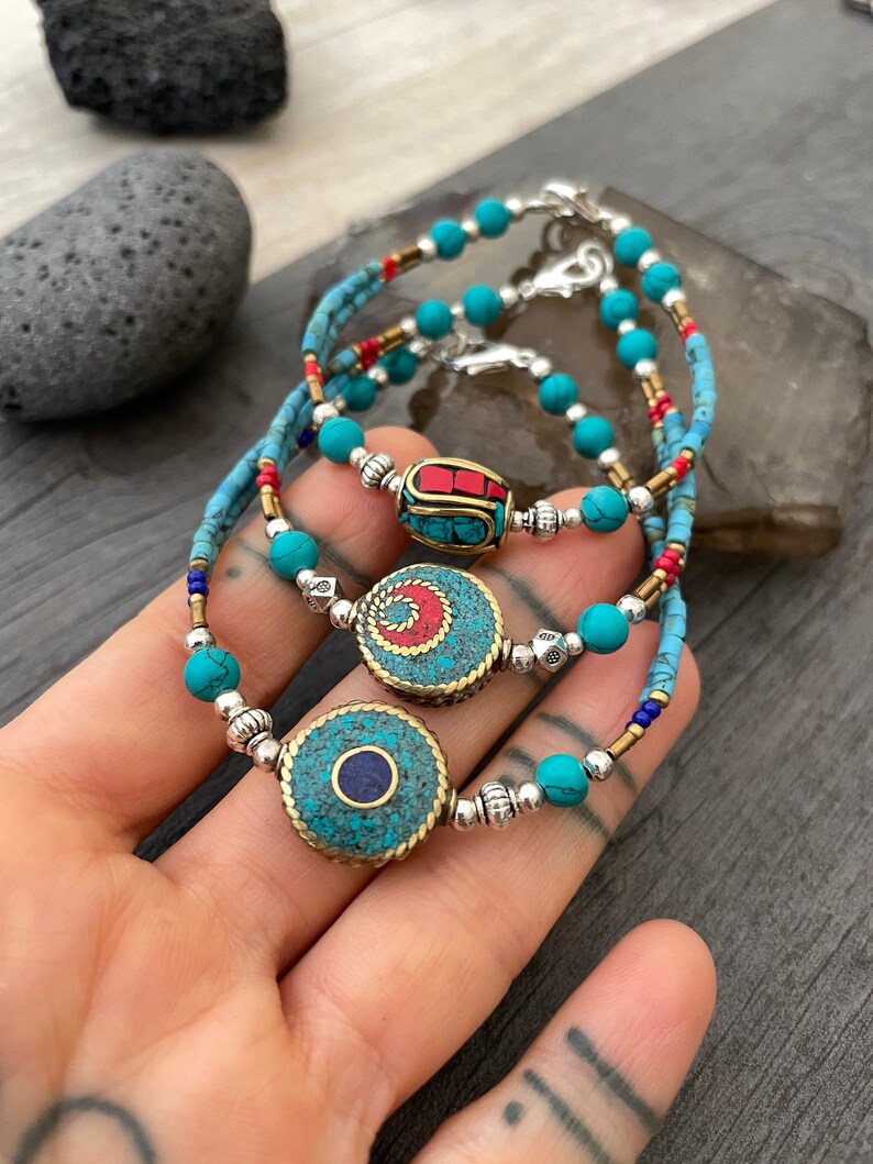 Puede incluir: Tres pulseras de cuentas turquesa con detalles plateados y dorados. Cada pulsera presenta un amuleto circular &uacute;nico con dise&ntilde;os intrincados y piedras turquesa, rojas y azules.