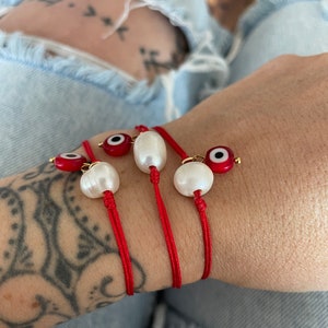 K&ouml;nnte beinhalten: Drei rote Armb&auml;nder mit wei&szlig;en Perlen und blauen und roten b&ouml;sen Augen.