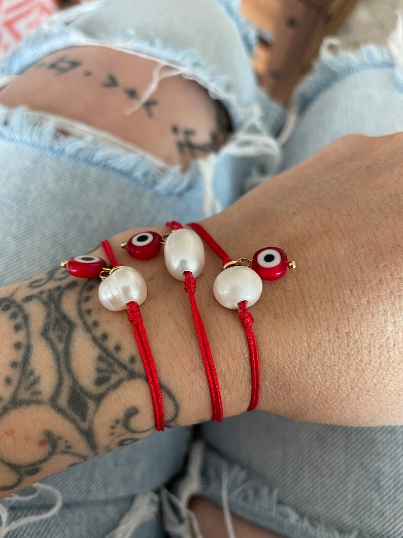 K&ouml;nnte beinhalten: Drei rote Armb&auml;nder mit wei&szlig;en Perlen und blauen und roten b&ouml;sen Augen.